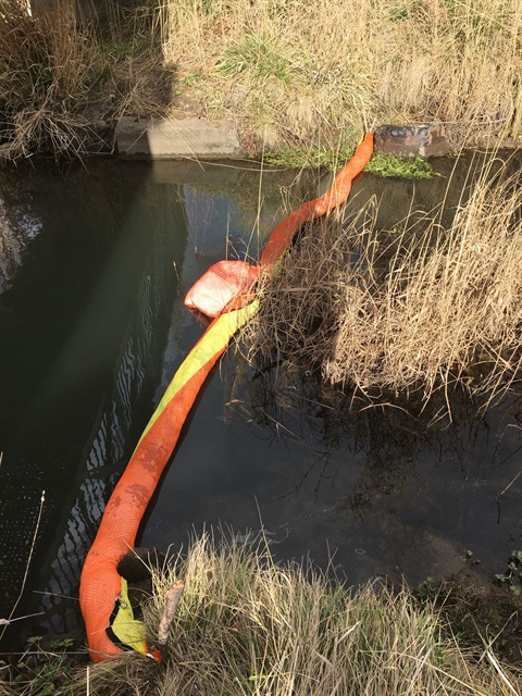 he third filtration boom in place in Cooma Creek. A chemical plume is visible on the left side of the boom, but absent on the right side (the direction of water flow).