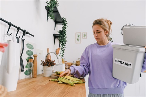 A young woman holding a kitchen organics caddy, about to place food scraps into the organics caddy.