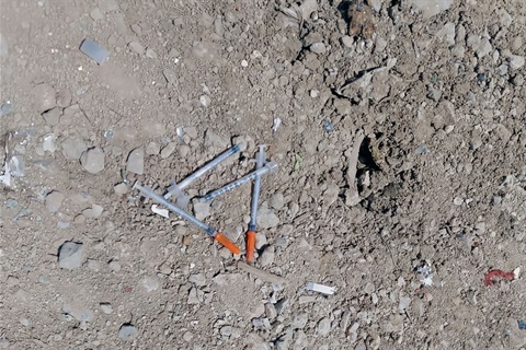 Used syringes on the ground at a public landfill waste drop-off location.