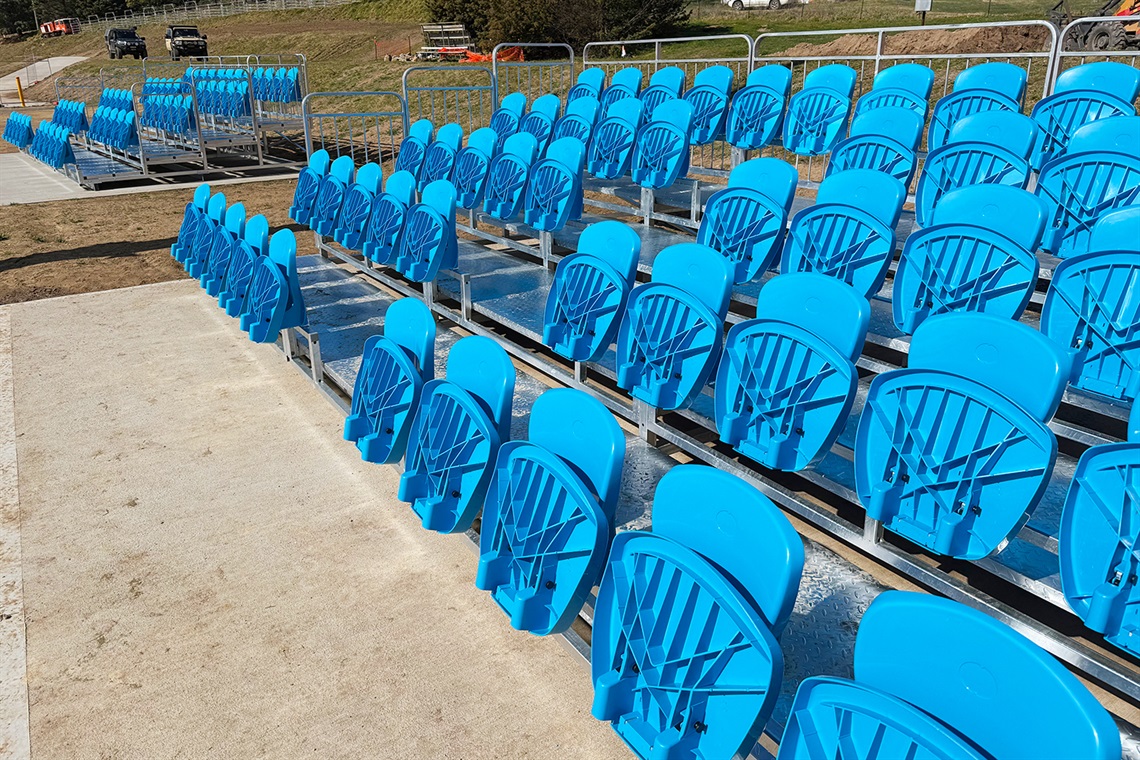 Bright blue stadium-style tiered seating sits freshly installed by brand new accessible pathways at Bombala Showground in August 2025