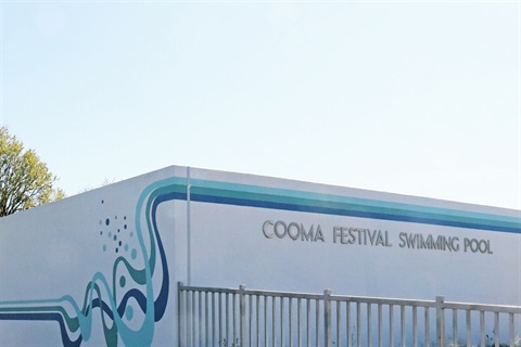 Close crop of a white-painted building with aquatic line motif, metal block-letter signage spells COOMA FESTIVAL SWIMMING POOL