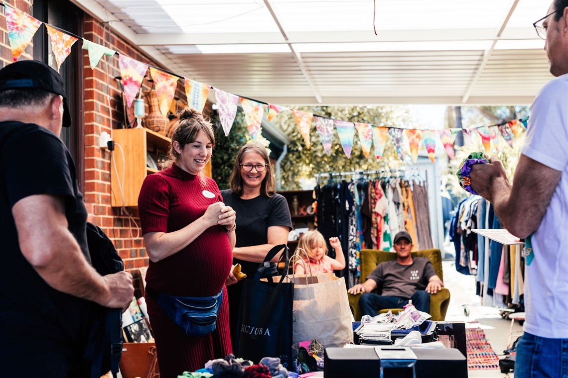 Garage Sale Trail sellers and buyers at a sale in carport at a suburban home