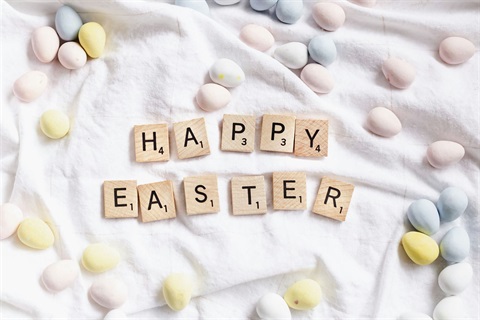Scrabble letters spelling out 'happy easter' on a tablecloth surrounded by Easter eggs.