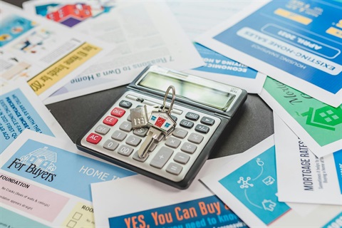 A set of keys with a design reading 'Home' engraved on the key, sitting atop a calculator and real estate and home buying related papers.