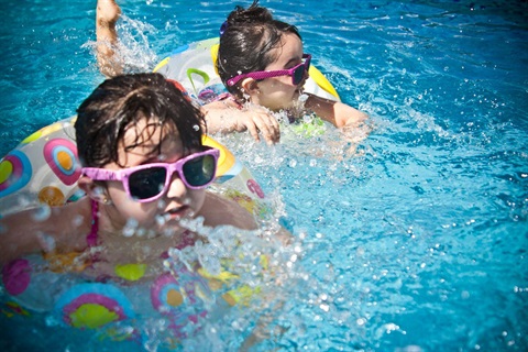 Young children swimming in a backyard pool with flotation devices