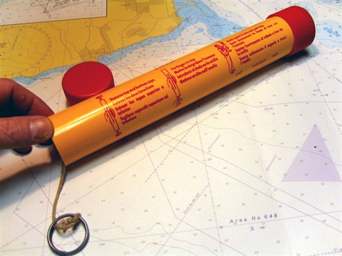 A marine parachute flare laid on top of a map, with a finger and thumb gripping its base 