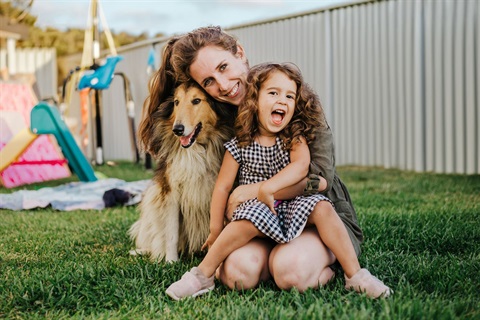 Mother, toddler-aged daughter and pet dog in backyard