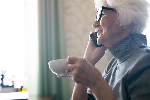 An older woman enjoying a phone call and cup of tea at home